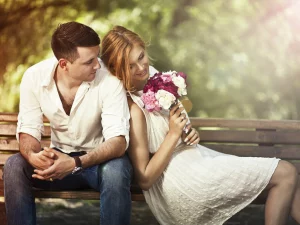 Due persone sedute vicino su una pancina e la ragazza ha in mano un mazzo di fiori