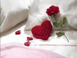L'immagine rappresenta un cuore rosso e una rosa poggiati su un letto