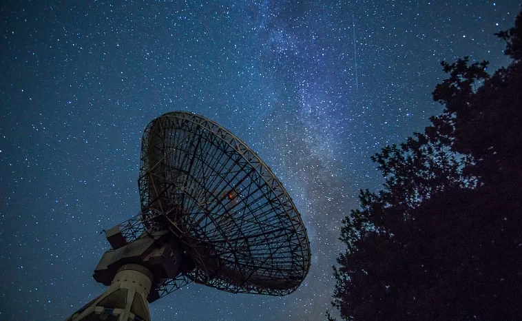 A radio telescope in front of a star-filled night sky, representing the scientific side of the astronomy vs astrology debate.